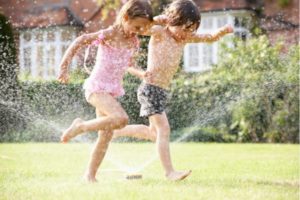 two kids running through the sprinklers
