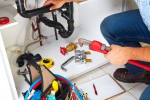 Plumber working under a sink with a lot of tools spread out