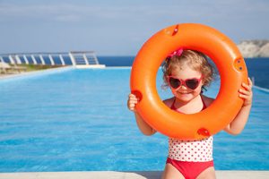 Little girl holding a pool float and standing near a pool